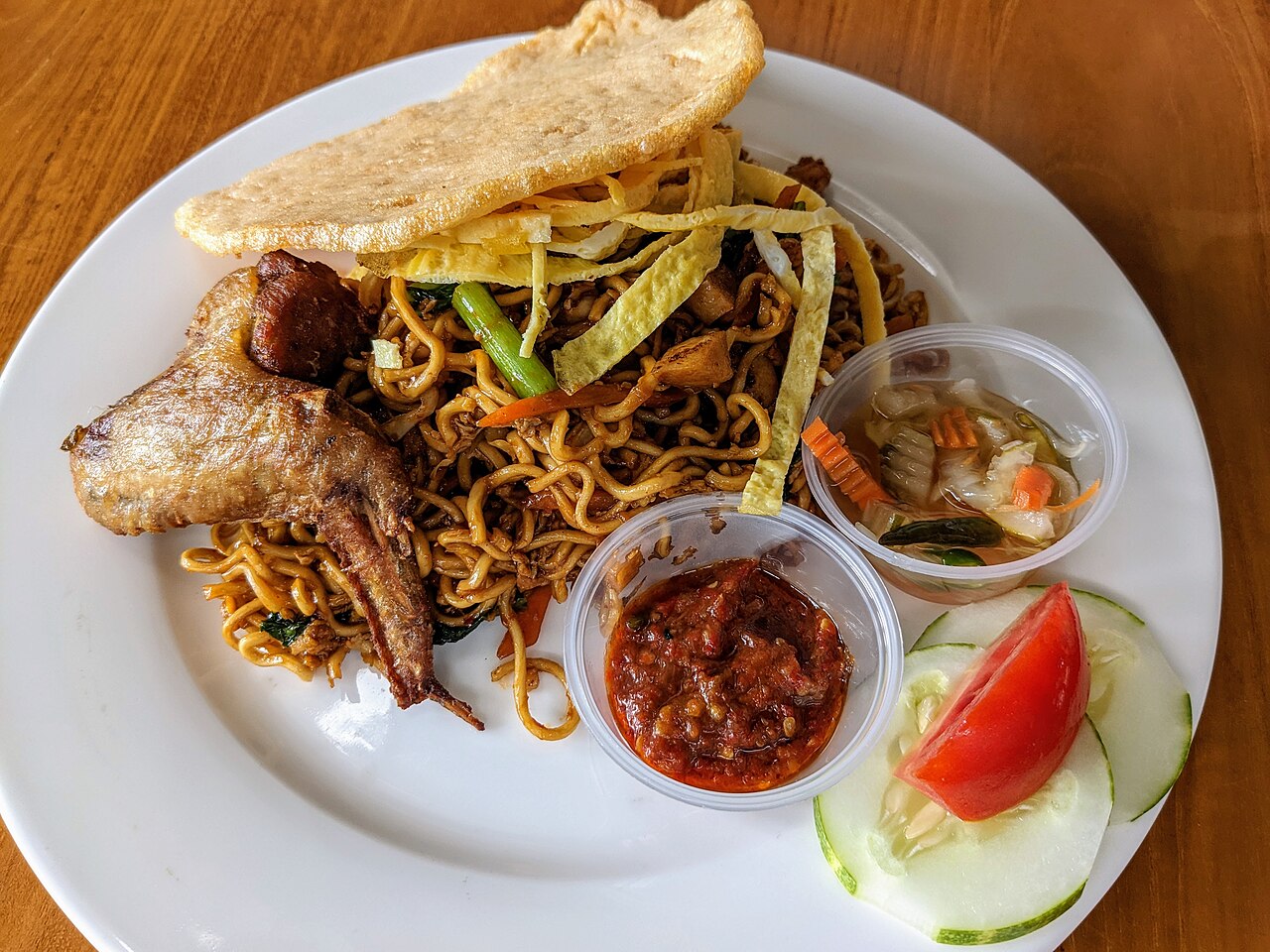 Fried noodles with egg strips, a grilled chicken wing, crackers, pickles and sambal