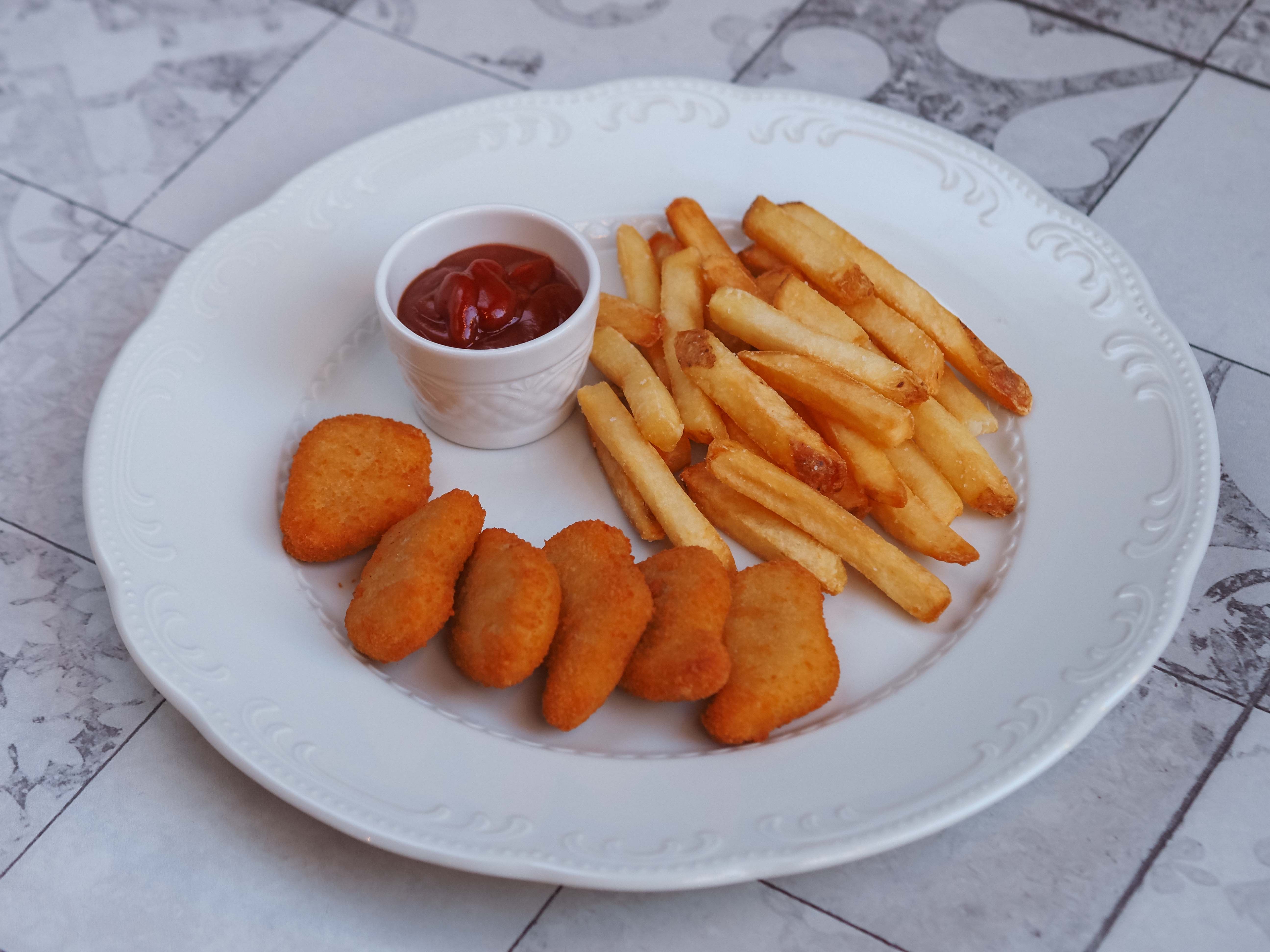 Chicken nuggets and golden fries on a white plate with a small pot of ketchup